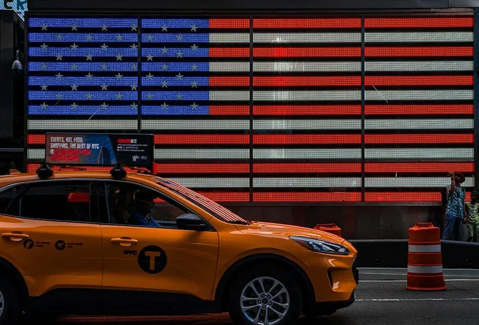 A yellow NYC cab with an American flag in lights behind it in New York, USA United States of America.