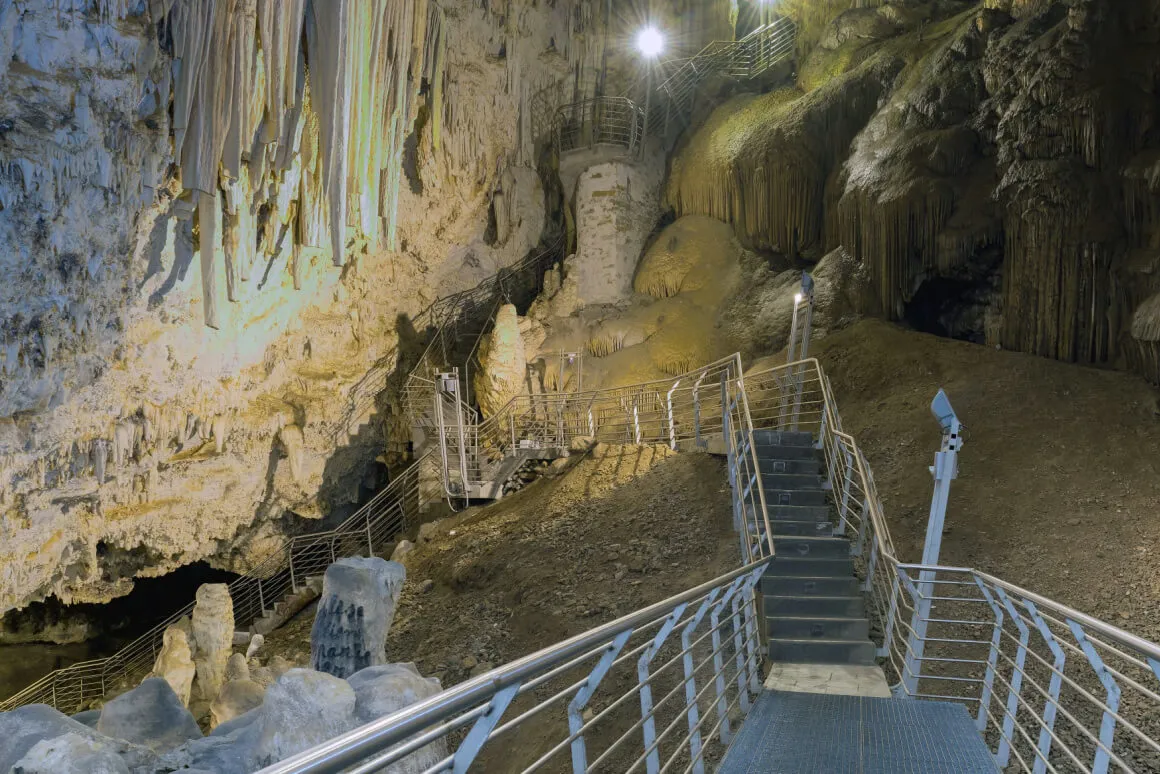 Staircase leading into a dark cave with geological formations in Antiparos
