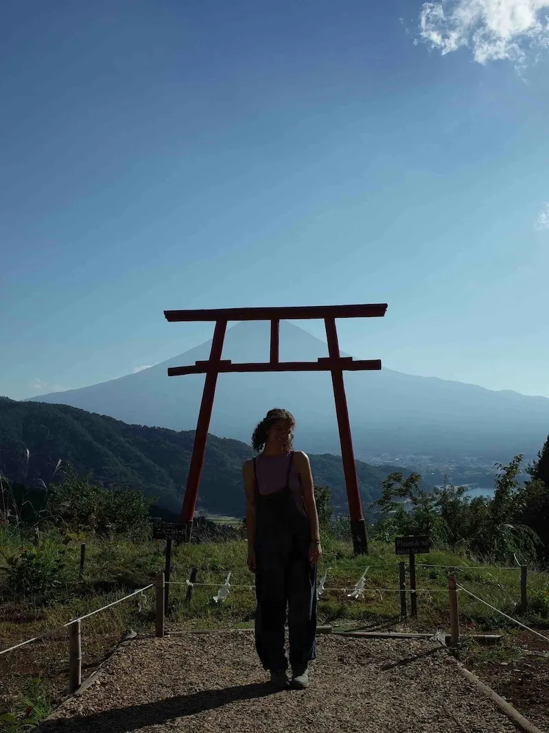 Girl poses for photo under shrine overlooking views of fuji-san.
