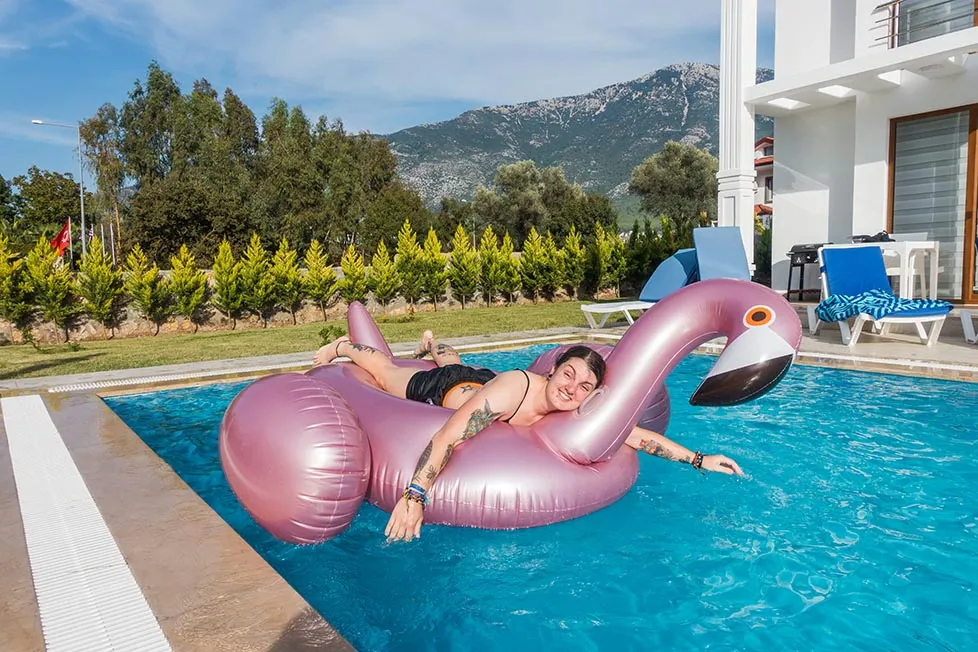Nic on an inflatable flamingo in a pool near a villa with mountains behind