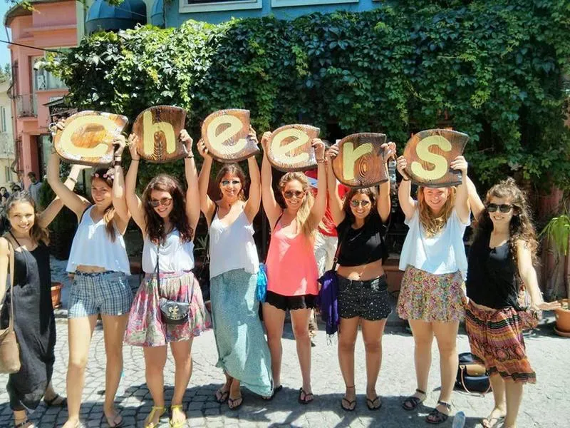 Girls holding up Cheers sign in front of ivy coveres building on the cobbled streets of Istanbul Cheers Hostel best hostels in Istanbul