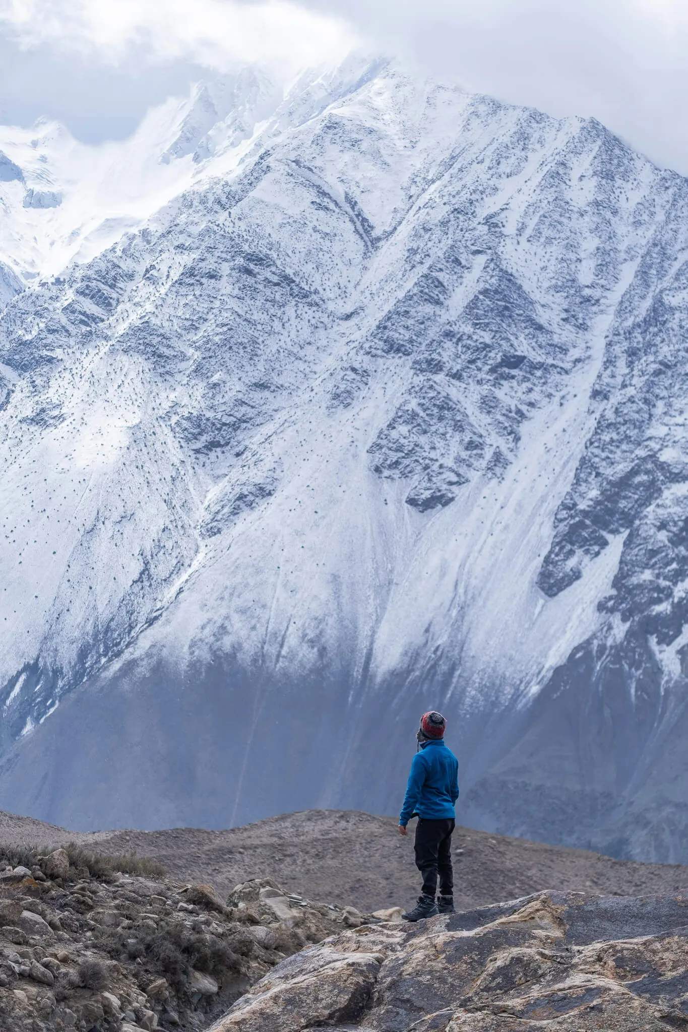 Will standing on a rock with a massive snow covered mountain behind him in Pakistan