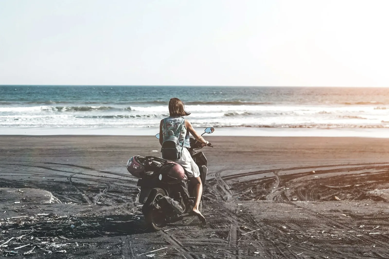 Young woman driving a scooter at the beach with black sand Bali Indonesia.
